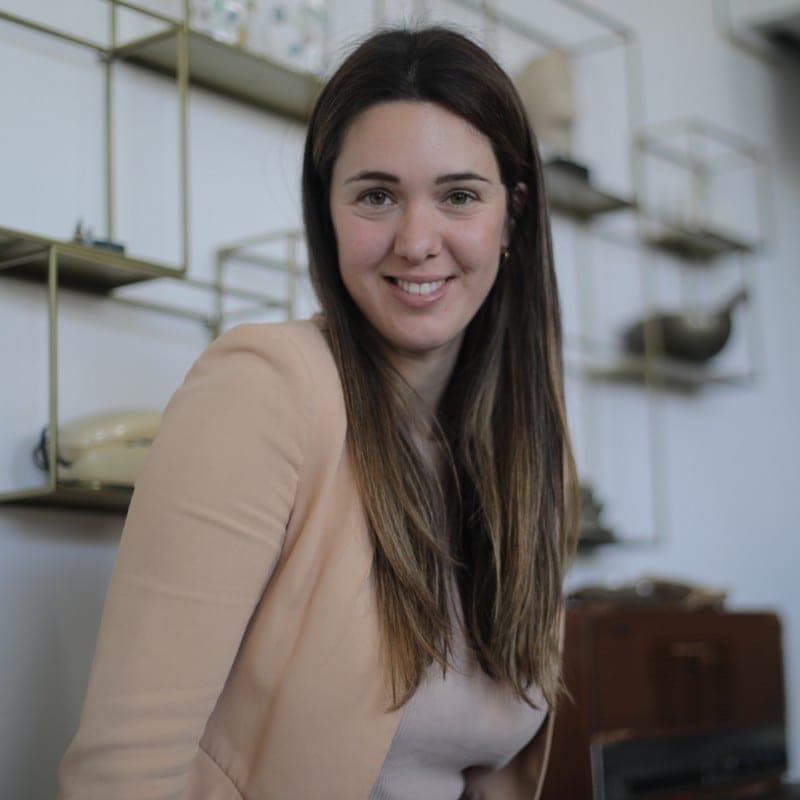 Retrato de Marta Martí, arquitecta, sonriendo en un interior con estanterías