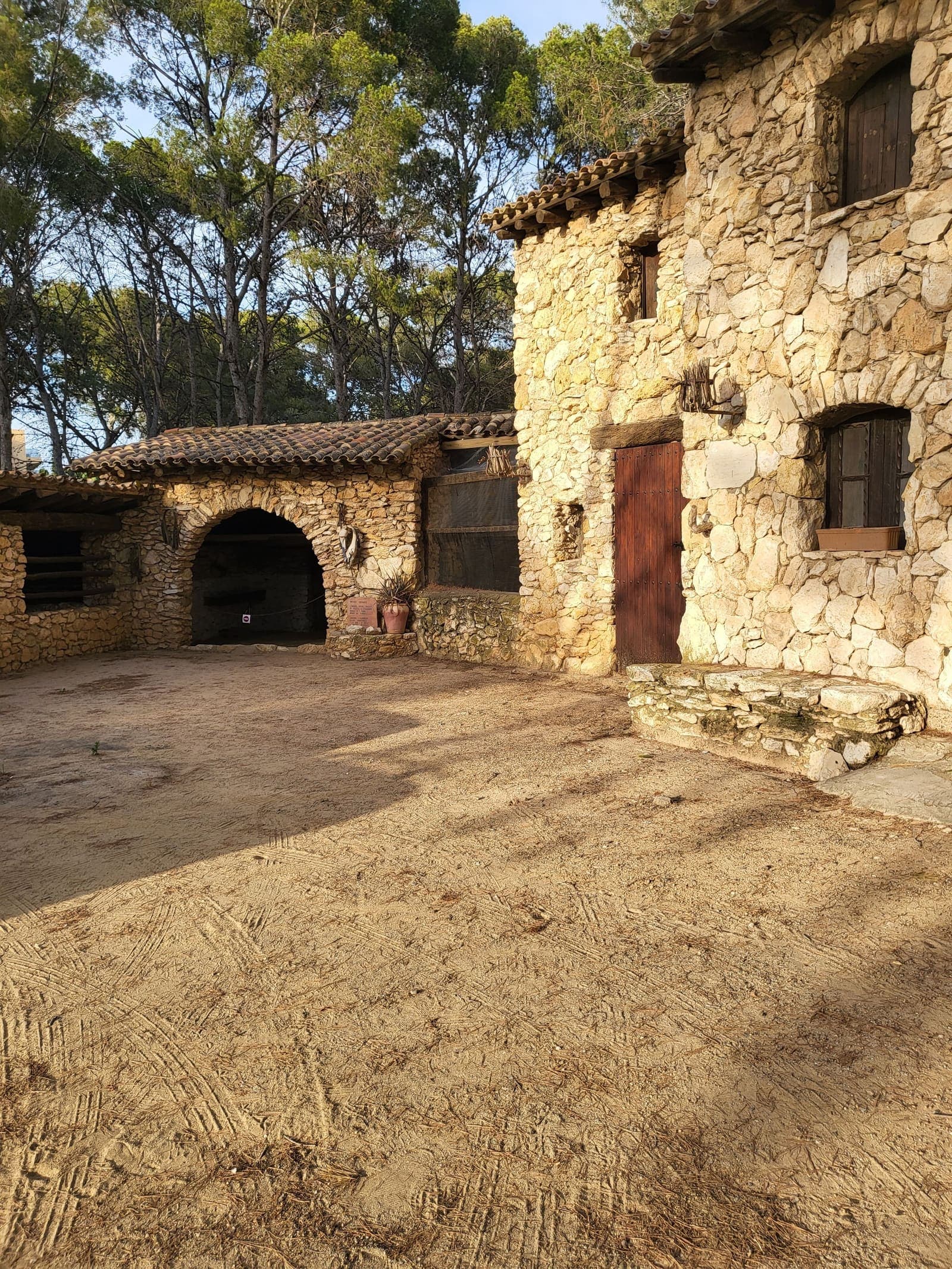 Pati de terra d'una masia catalana de pedra envoltada de pins